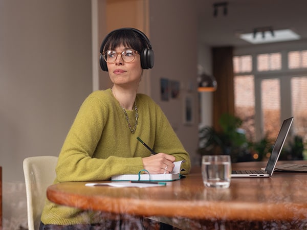 En person som bär bekväma Philips hörlurar sitter vid ett bord med en anteckningsbok och en laptop