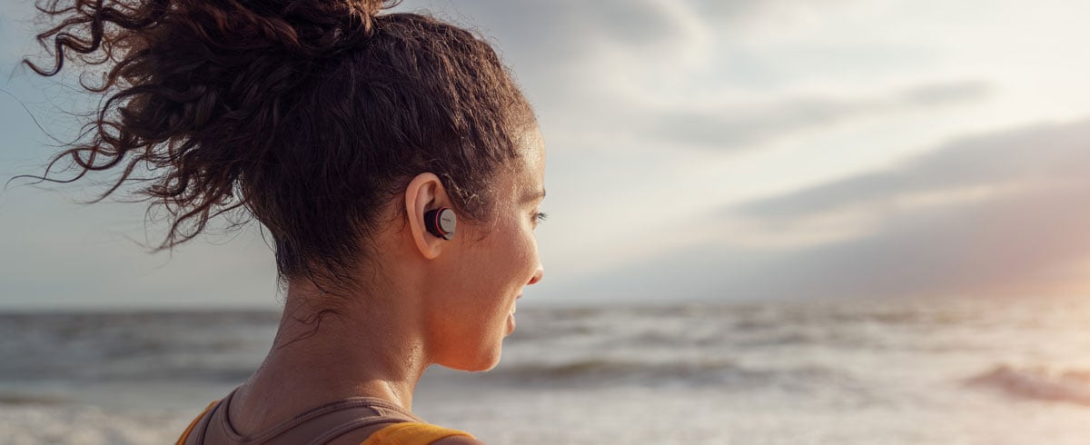 Kvinna som använder true wireless-hörlurar vid havet