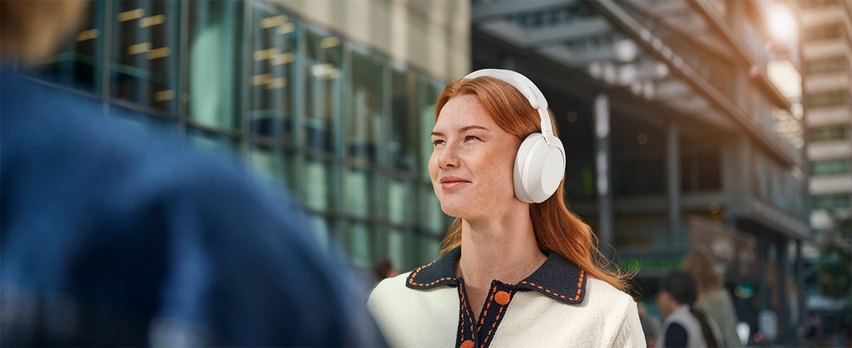 Person som bär Philips TAH8000EWT over-ear hörlurar utomhus i en urban miljö