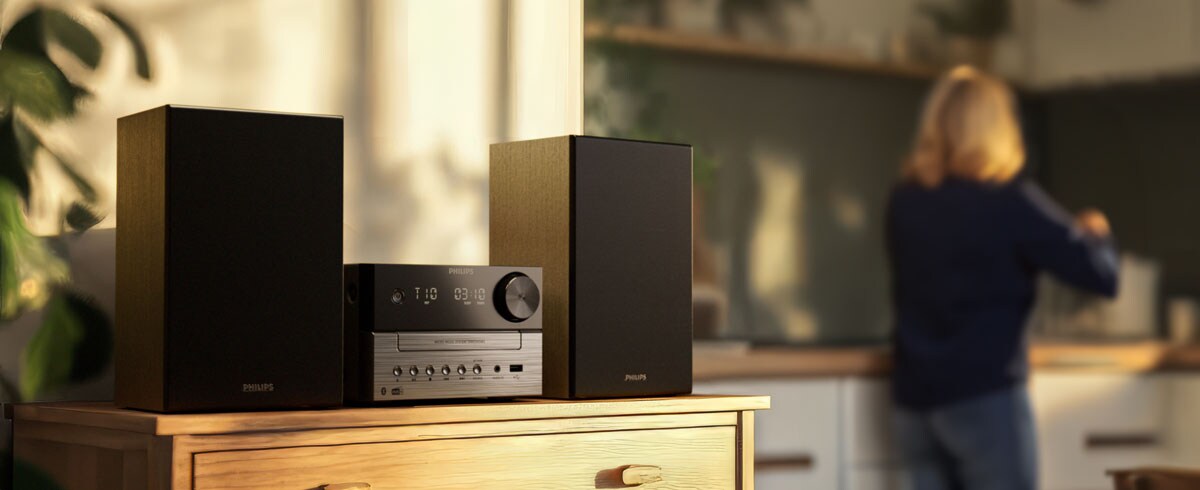 Kvinna som lyssnar på musik i köket med ett musiksystem från Philips