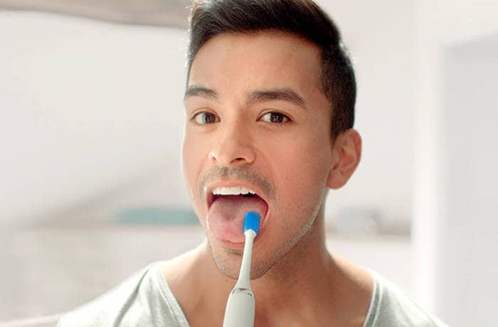 En man rengör sin tunga med en speciell tungborste från Philips. 