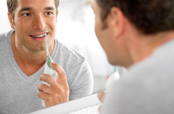En man tittar på sin spegelbild medan han borstar sina vita tänder med en elektrisk tandborste.