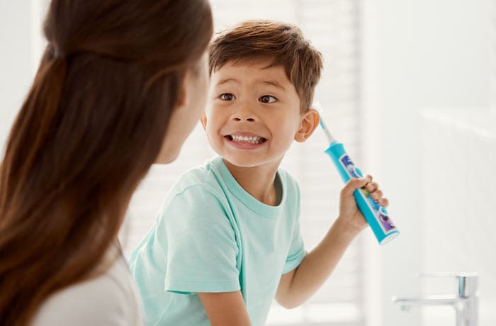 En ung pojke ler mot sin mamma medan han håller i en blå Philips Sonicare for Kids-tandborste.