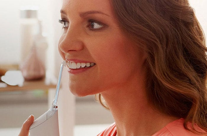 En kvinna borstar sina kritvita tänder med Philips Sonicare Airfloss eltandborste.
