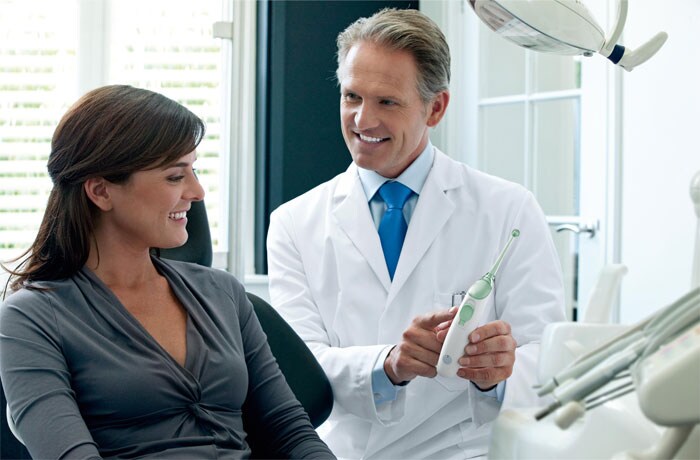 En tandhygienist visar den interdentala tandborsten Philips Sonicare AirFloss för sin patient.