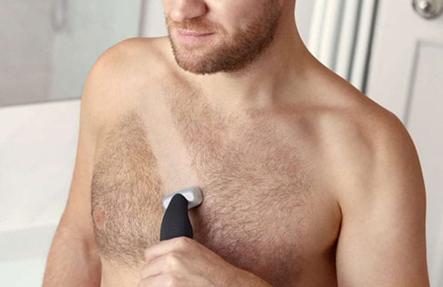 Överkroppen på en man som rakar en linje av sitt brösthår med en rakhyvel.