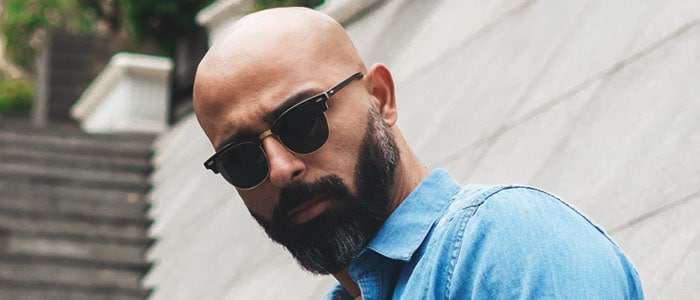 En skallig man med mörkt, lätt grånat skägg som bär svarta solglasögon och en blå jeansskjorta.