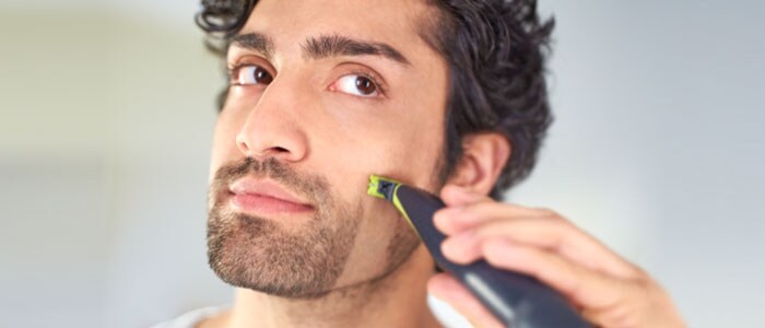 Bild av en man med mörkt hår och mörkt skägg som rakar sidan av sitt skägg.