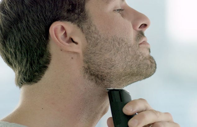 En man rakar sin skägglinje med en elektrisk skäggtrimmer från Philips.