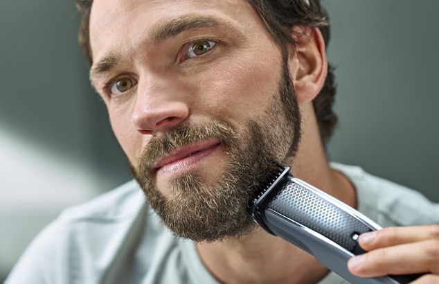 En man trimmar sitt skägg med en elektrisk rakapparat.