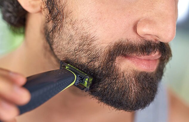 Undre delen av en mans ansikte som trimmar sitt skägg med en OneBlade-rakhyvel.
