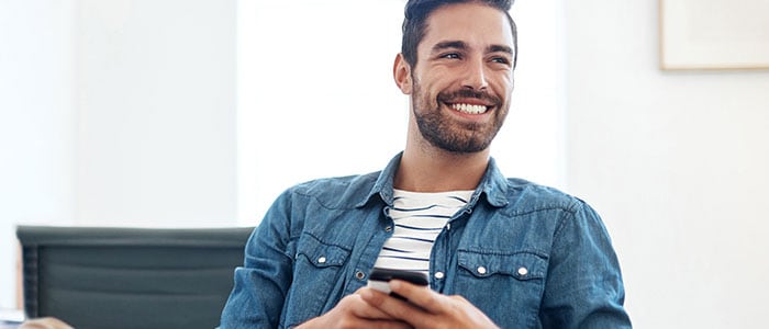 En leende man i skjorta med skäggstubb håller i en telefon.
