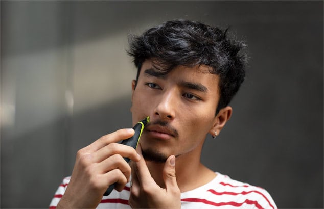 En ung man i en röd- och vitrandig t-shirt trimmar sin mustasch med Philips OneBlade.