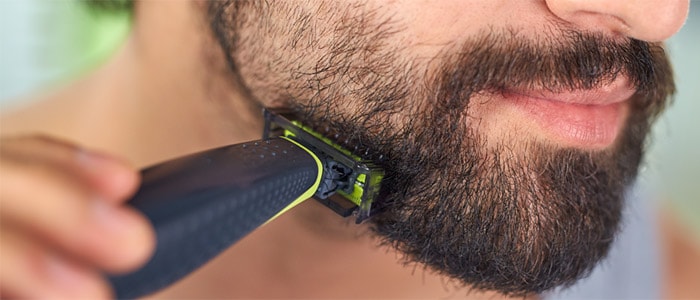 Närbild av en brunögd man som rakar sig och trimmar sitt mörka skägg med Philips OneBlade.
