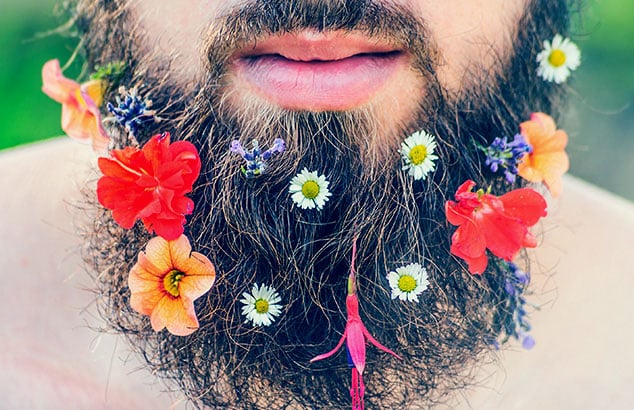 Närbild av en mans långskägg pyntat med olika blommor. 