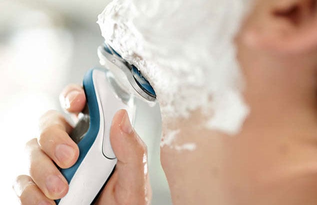 En man rakar sig med en vattentålig elektrisk rakhyvel och raklödder.