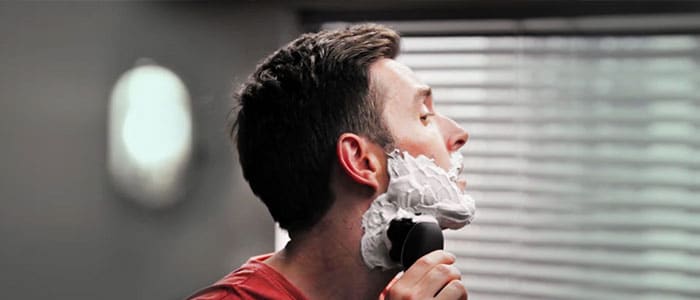 Sidoprofil av en man som rakar sig med en elektrisk rakapparat.